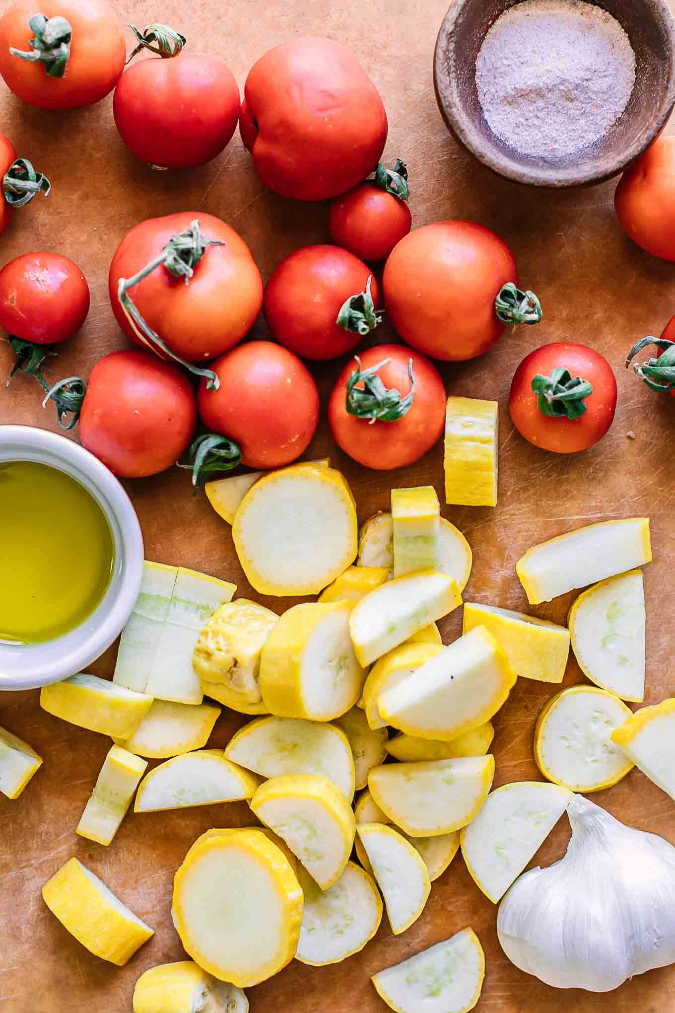 cherry tomatoes and sliced yellow summer squash on a wood cutting board