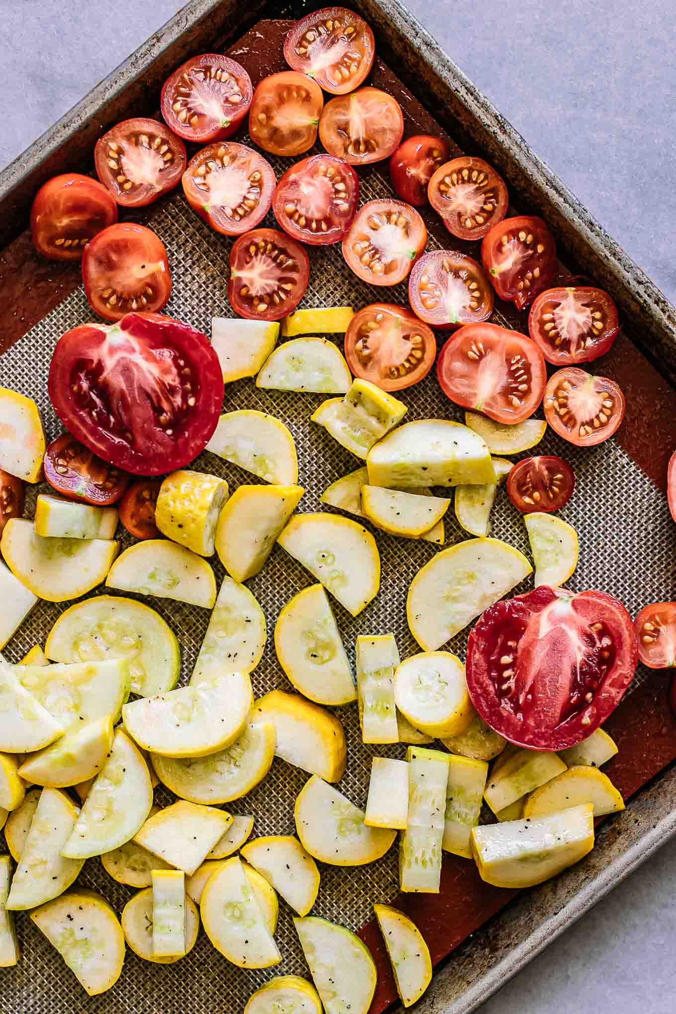 sliced summer squash and tomatoes on a roasting pan