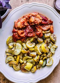 roasted summer squash and tomatoes on a white plate on a wood table
