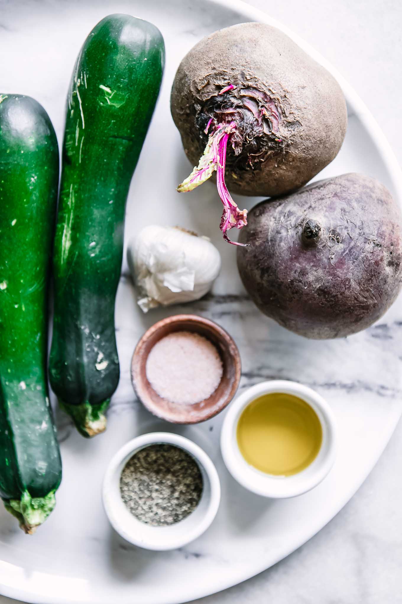 zucchini, red beets, garlic, and bowls of oil, salt, and pepper on a white table