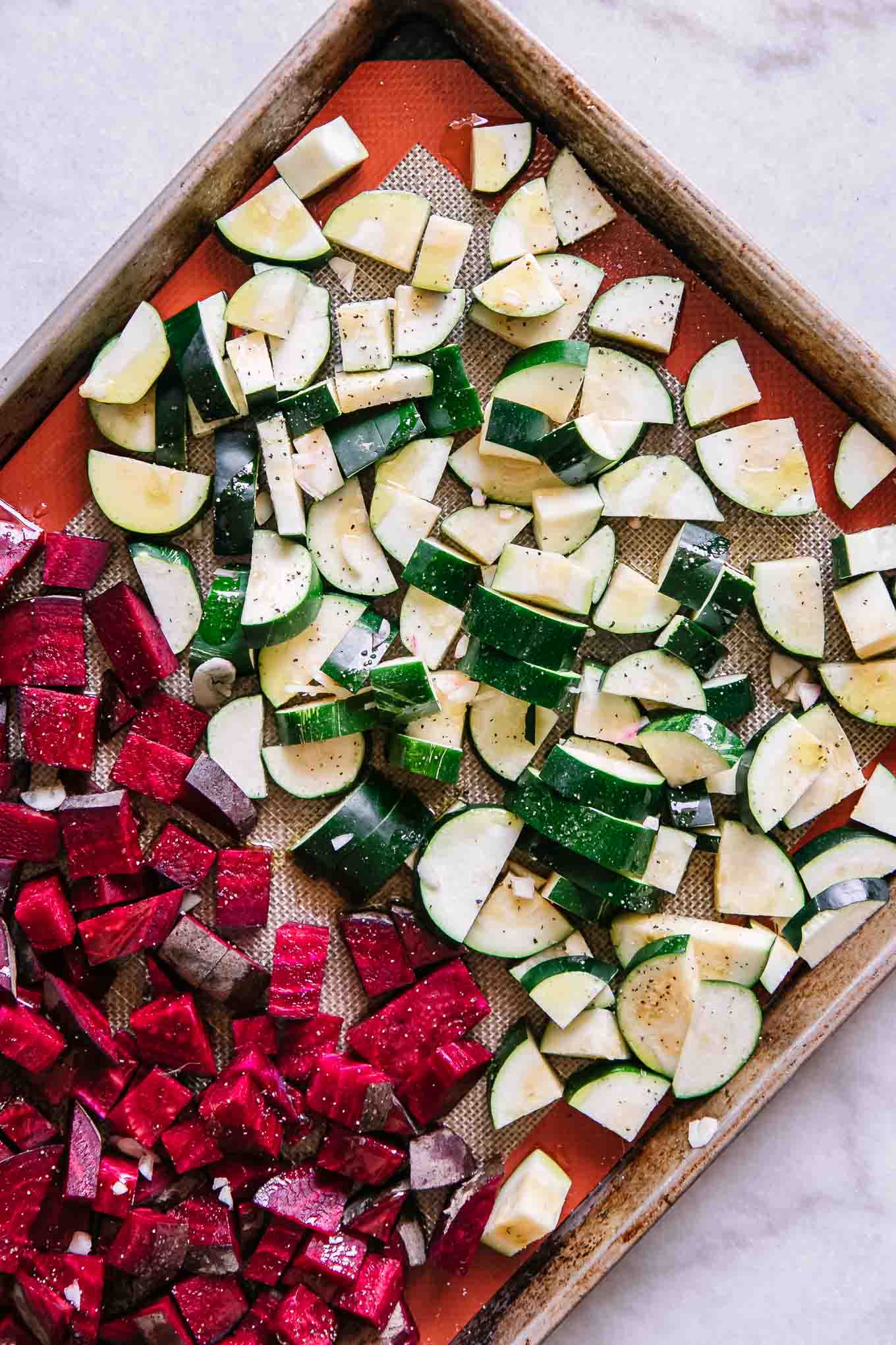 sliced and seasoned beets and zucchini on a baking sheet before roasting