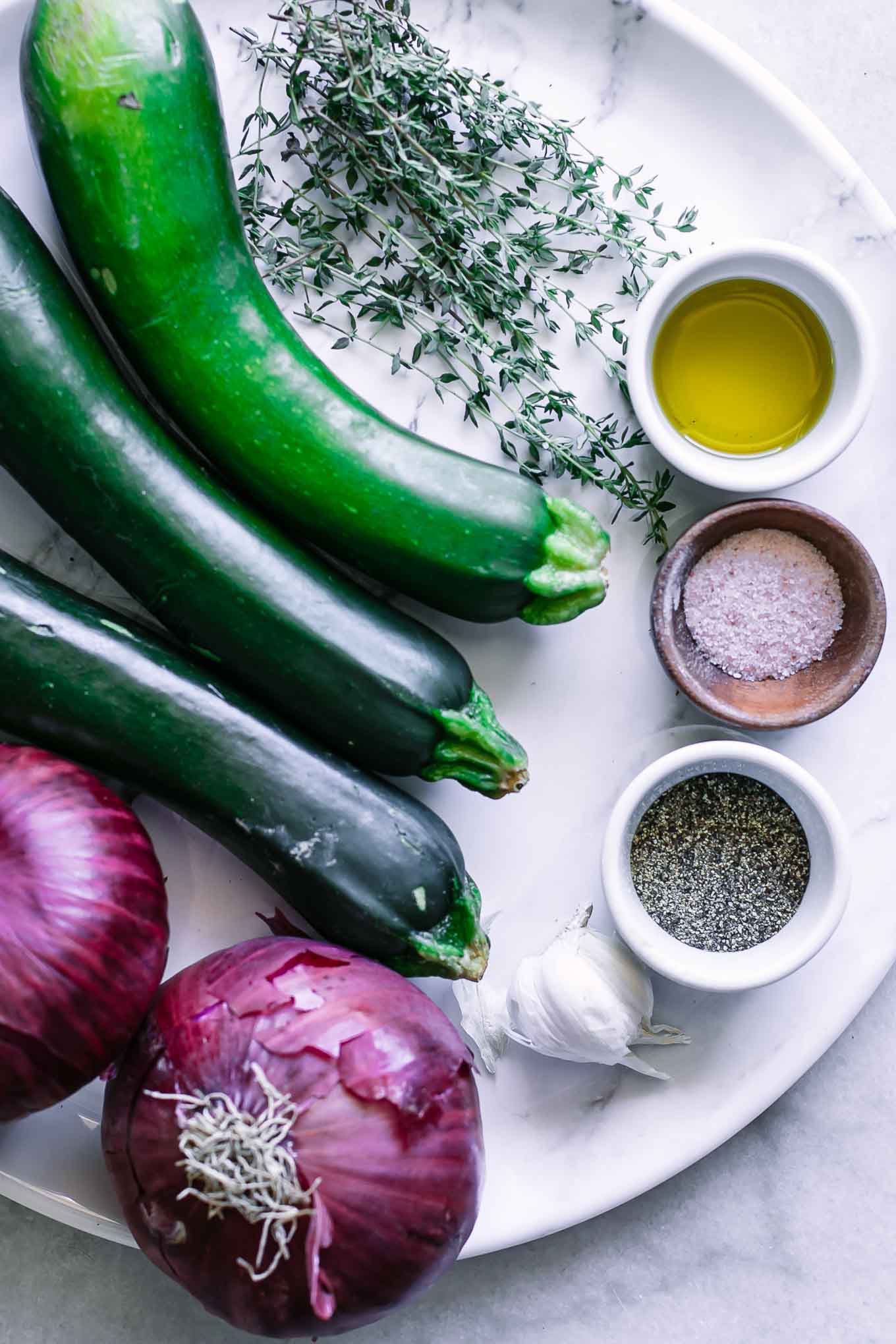 zucchini, red onions, garlic, olive oil, salt, and pepper on a white plate