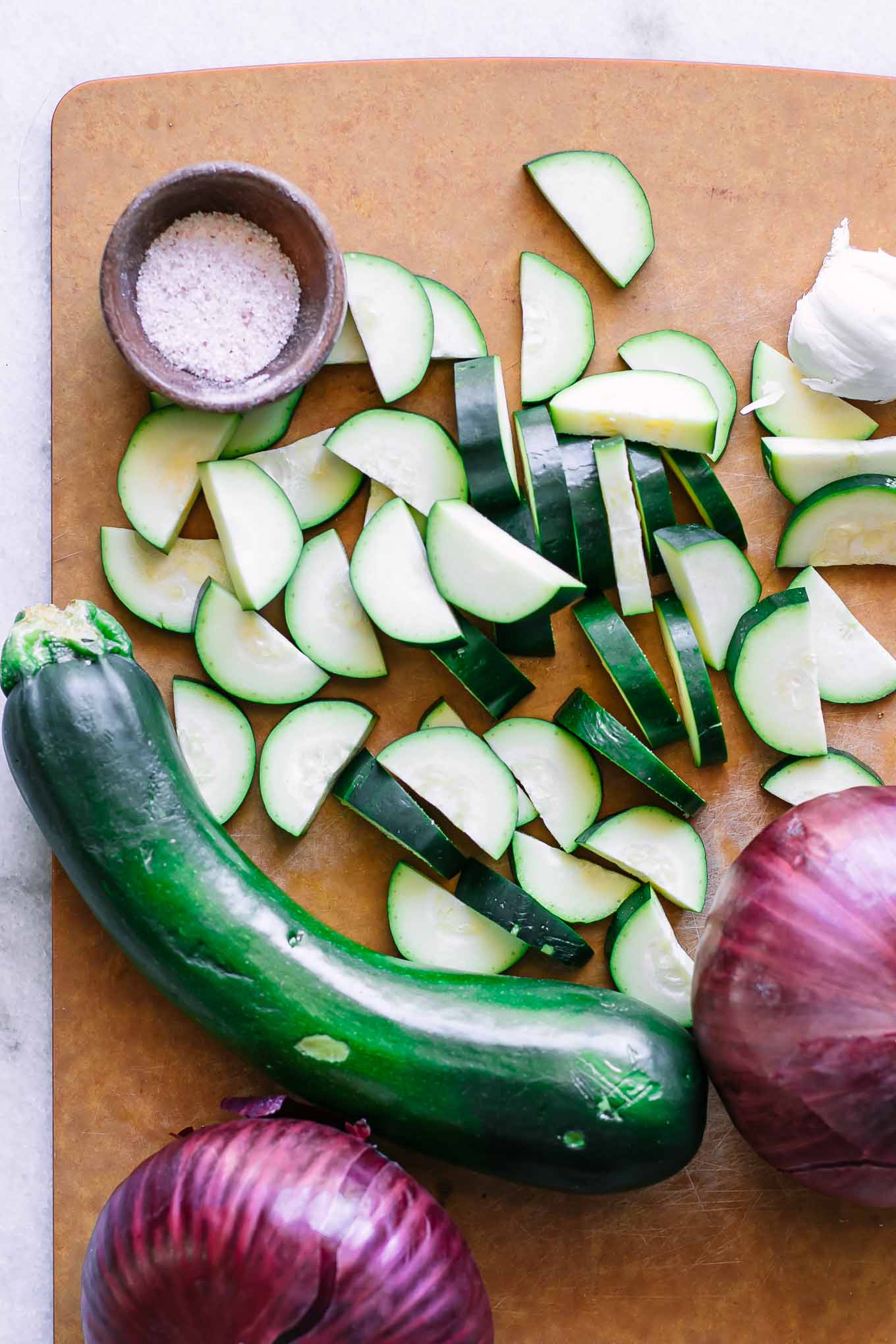 sliced zucchini and red onions on a wood cutting board