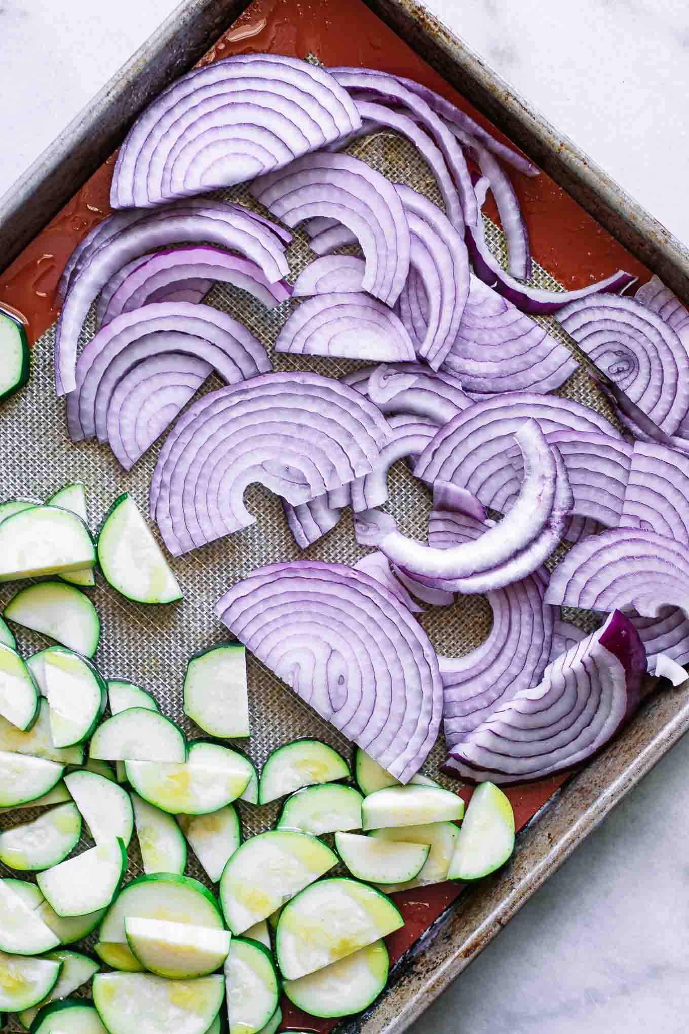 sliced red onion and zucchini on a roasting pan before baking