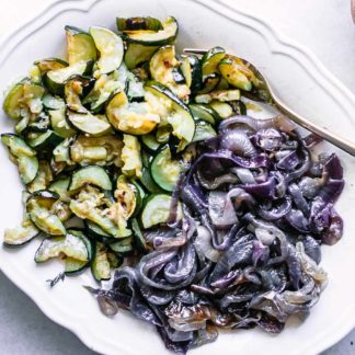 a plate of baked zucchini and onions on a white table with a gold fork