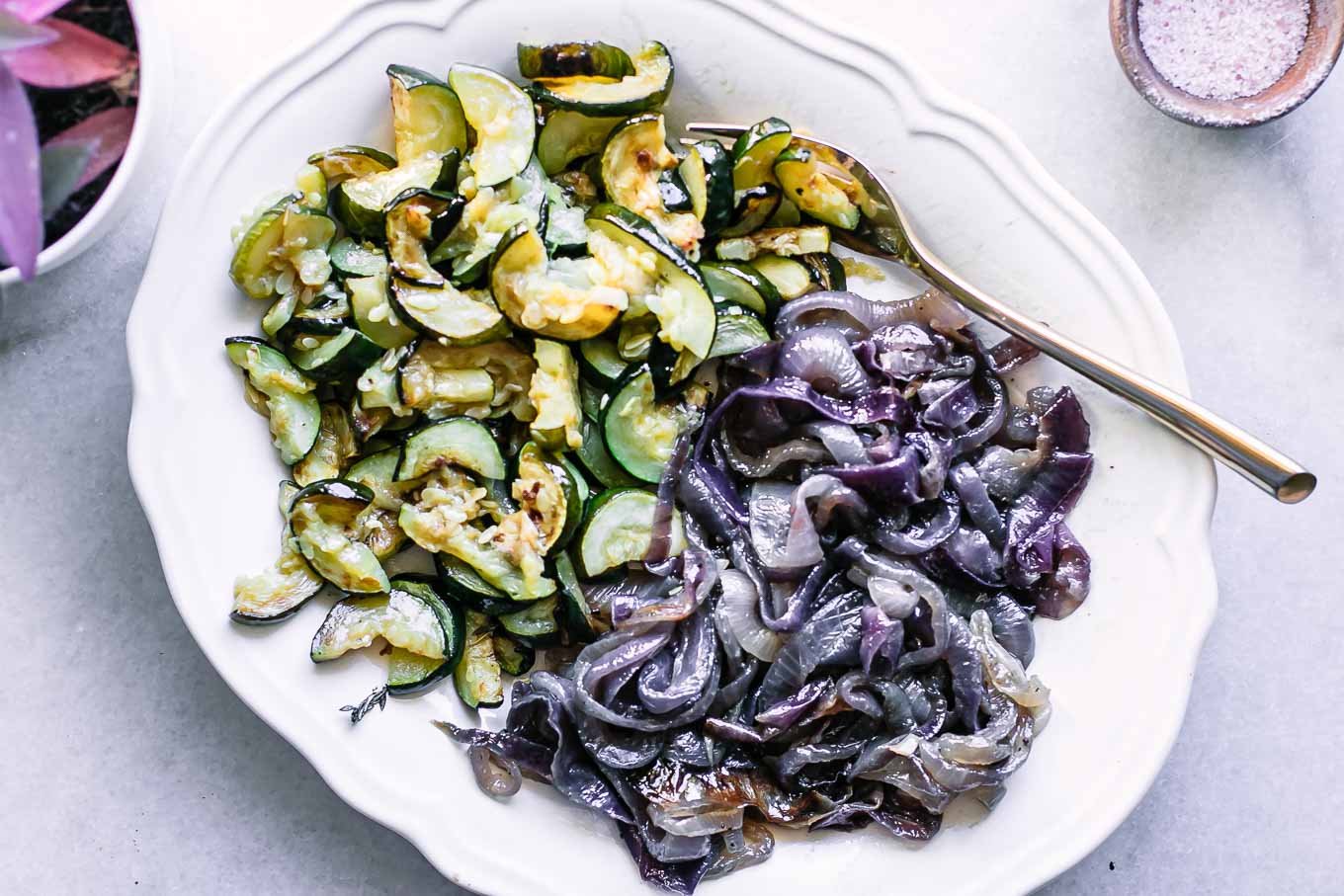 a plate of baked zucchini and onions on a white table with a gold fork