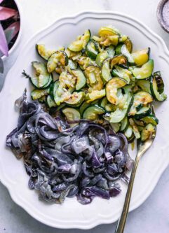roasted zucchini and red onions on a white plate on a white table