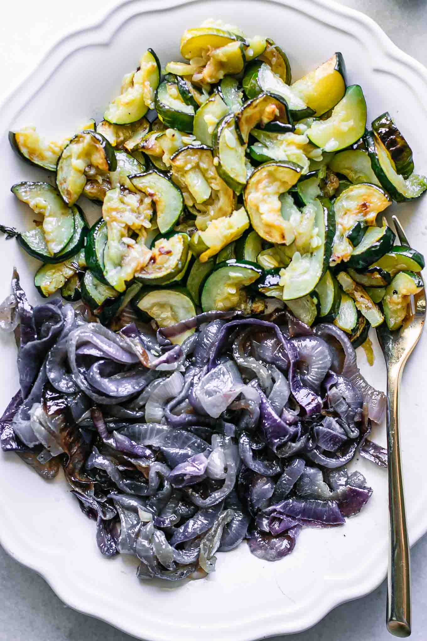 a close up of roasted zucchini and red onion slices on a white plate