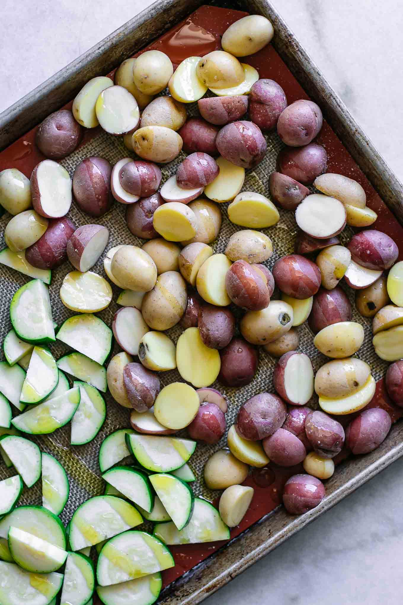 sliced potatoes and zucchini on a baking sheet before roasting