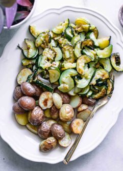 roasted zucchini and potatoes on a white side dish plate on a white table with a gold fork