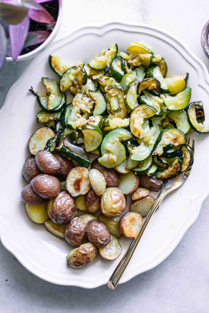 roasted zucchini and potatoes on a white side dish plate on a white table with a gold fork