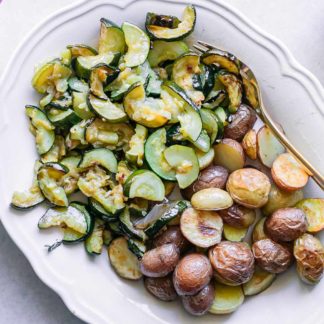 roasted zucchini and potatoes on a white plate on a white table