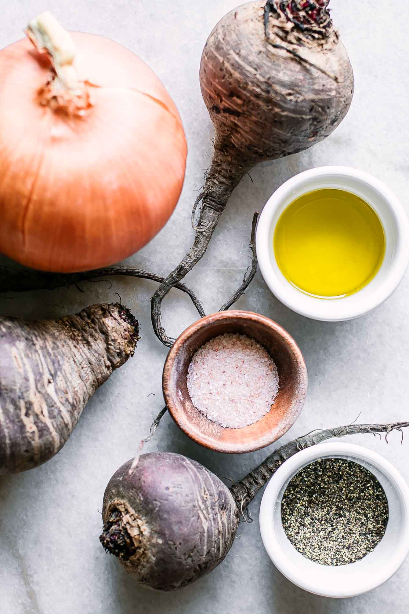 beets, an onion, and bowls of olive oil, salt, and pepper on a white countertop