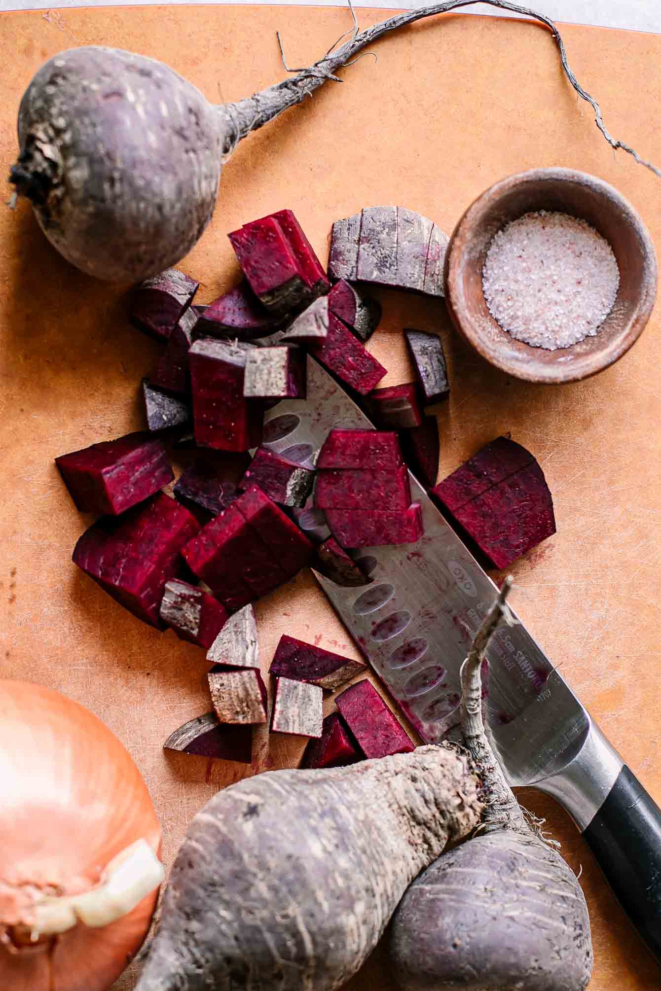 cut red beets on on an cutting board with an onion and a knife
