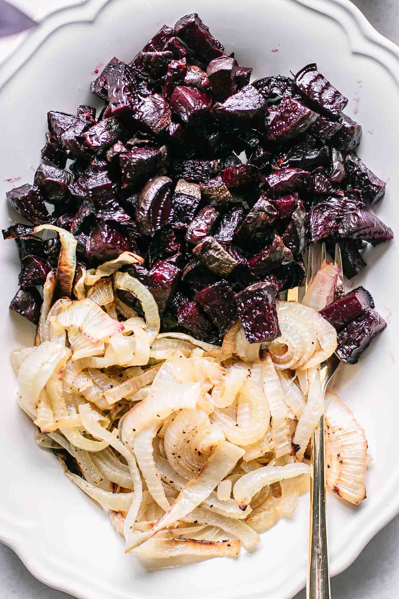 a close up of baked beets and roasted yellow onions on a white plate