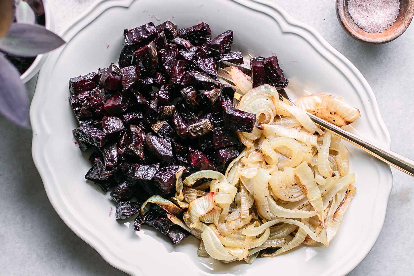 baked onions and beets side dish on a white table with a gold fork
