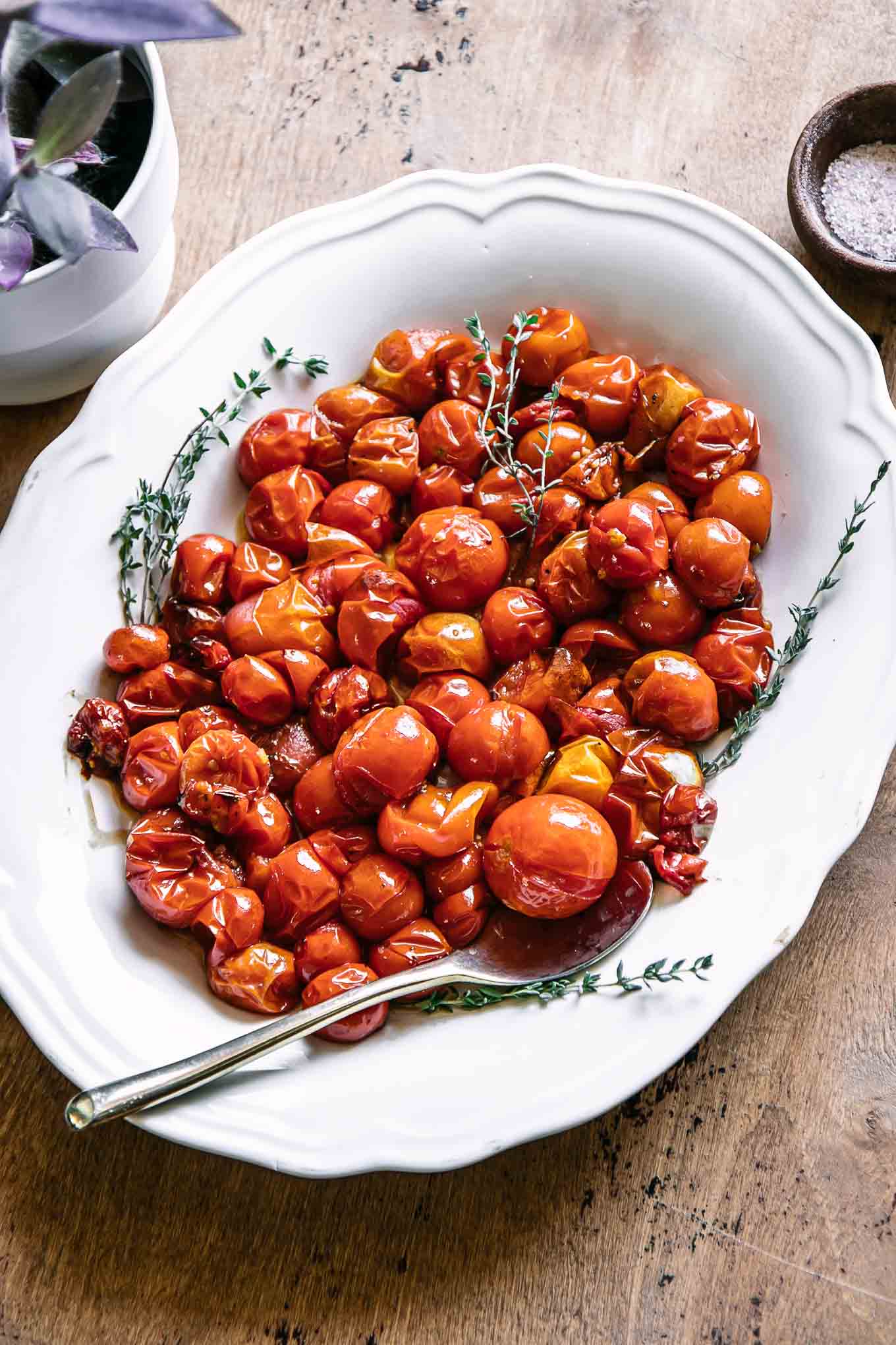 burst cherry tomatoes on a white plate with a gold fork on a wood table