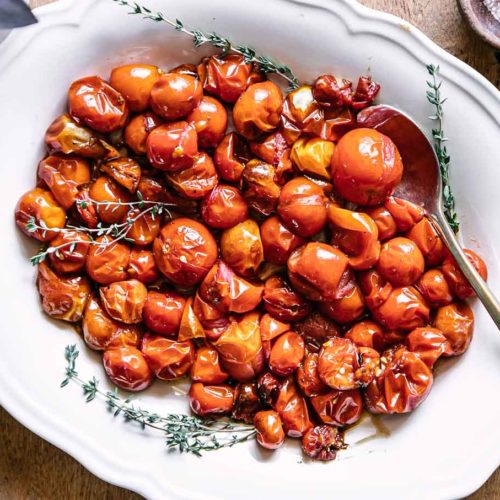 baked cherry tomatoes on a white plate on a wood table
