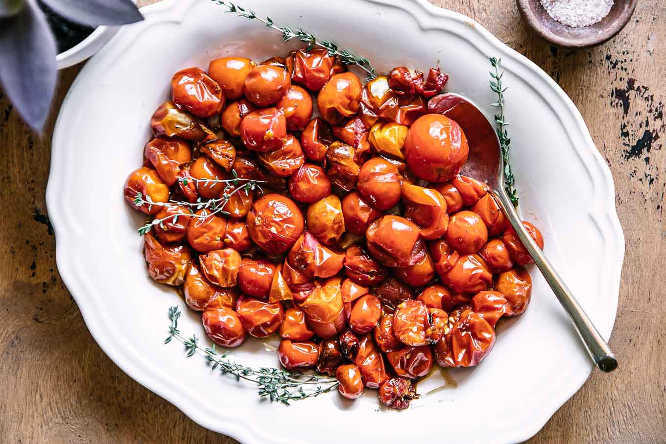 baked cherry tomatoes on a white plate on a wood table