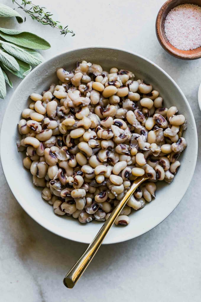 a side dish with black eyed peas and fresh herbs on a white table