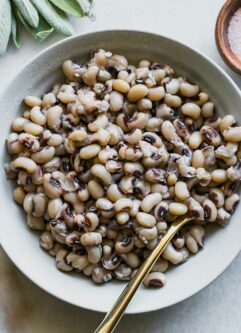 a bowl of cooked black eyes peas with a gold fork on a white table