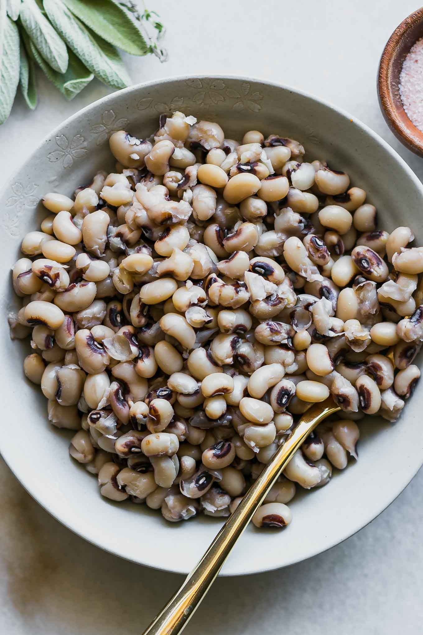 a bowl of cooked black eyes peas with a gold fork on a white table