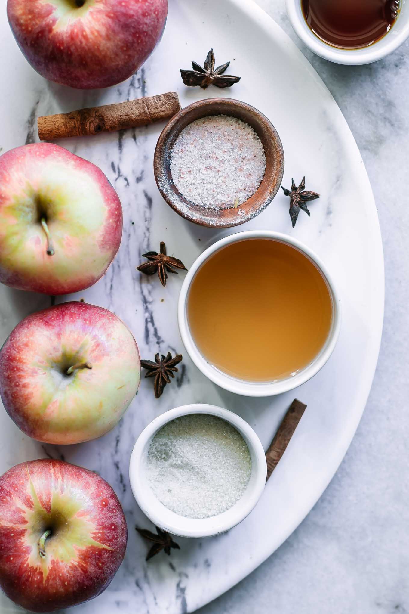 apples and bowls of apple cider vinegar, sugar, salt, vanilla, and water on a white table