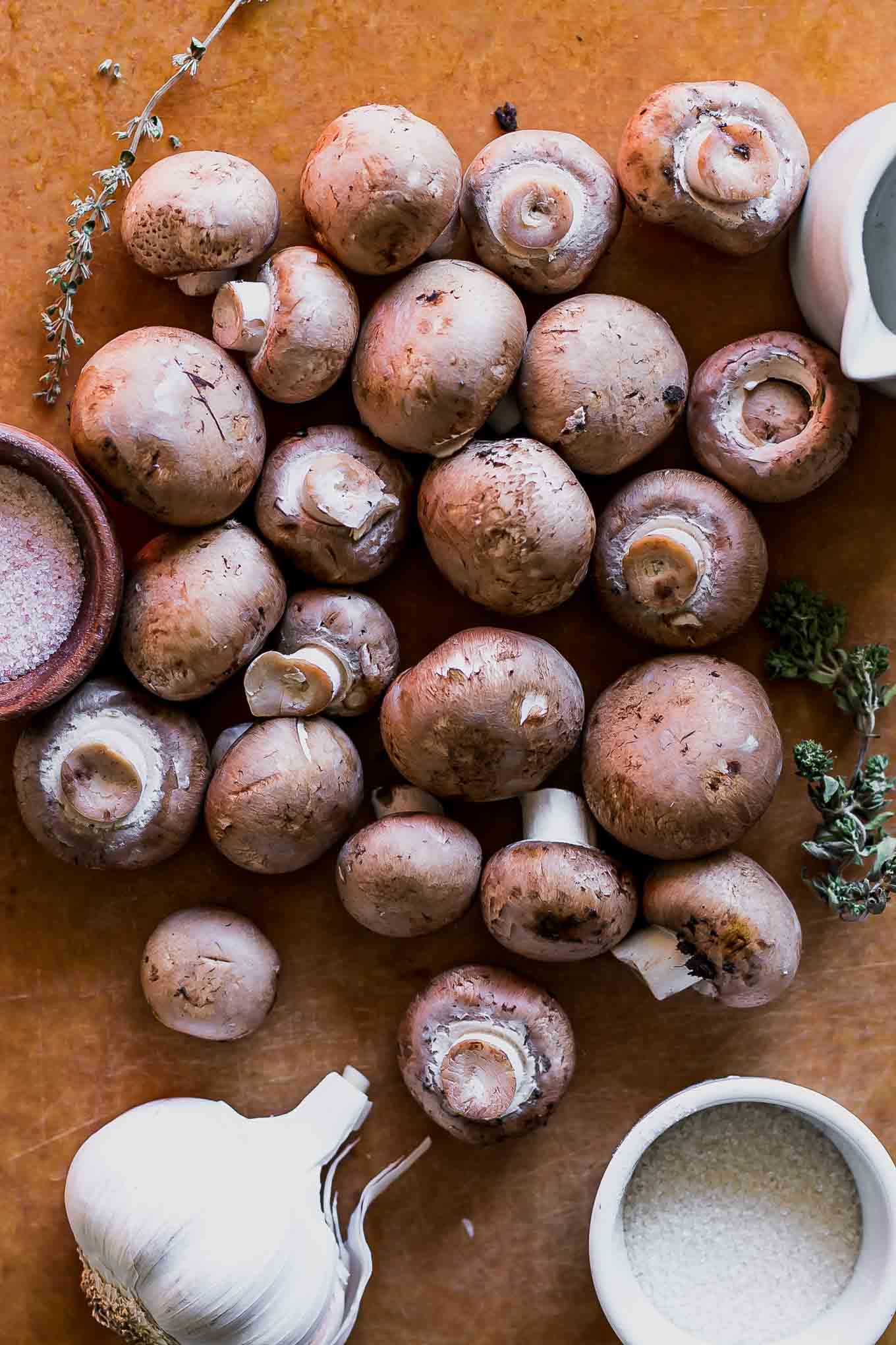 small button mushrooms on a wood cutting board with garlic