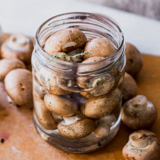 quick pickled mushrooms in a jar with vinegar brine on a wood table