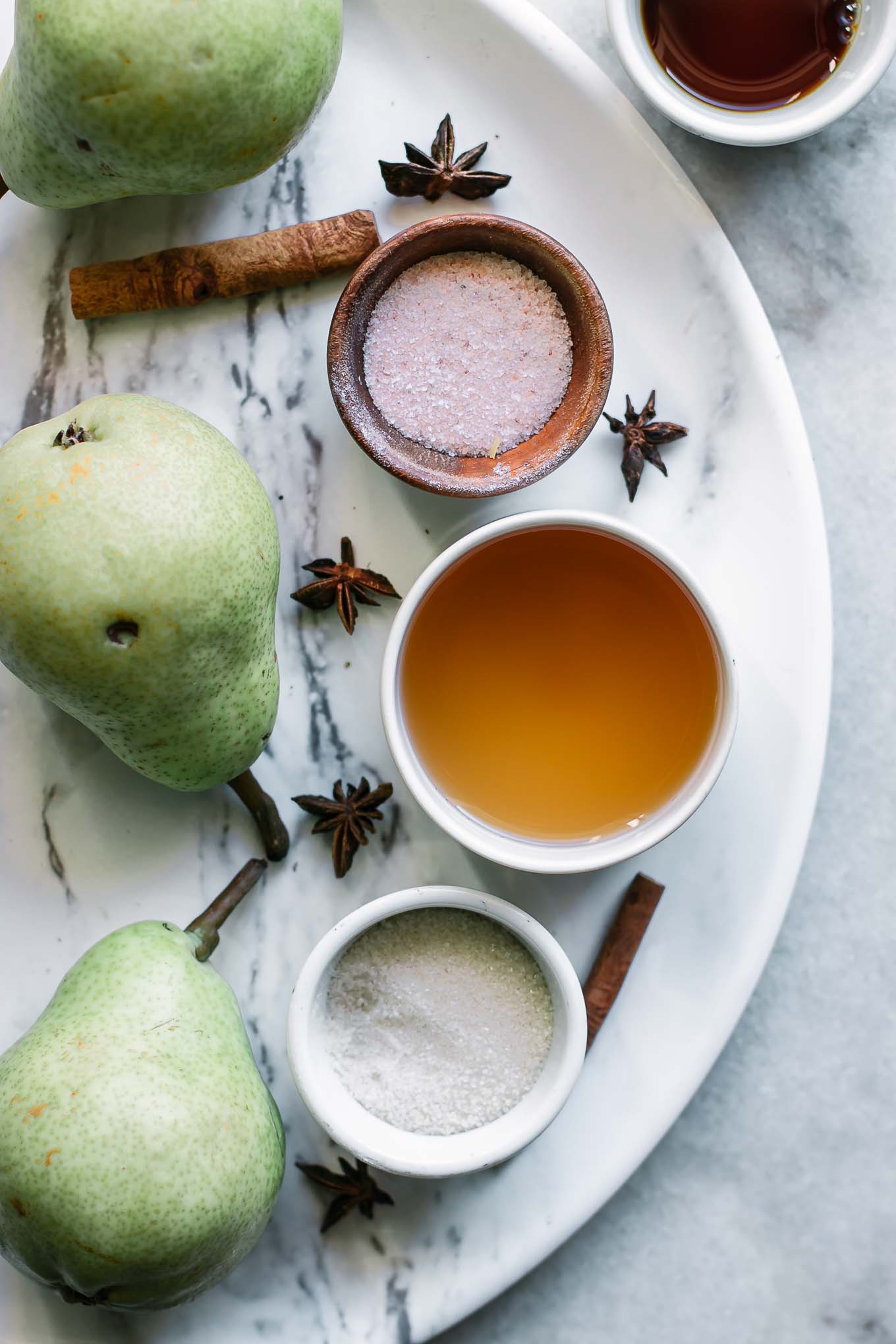 pears and bowls of water, vinegar, vanilla, sugar, and cinnamon before pickling on a white table