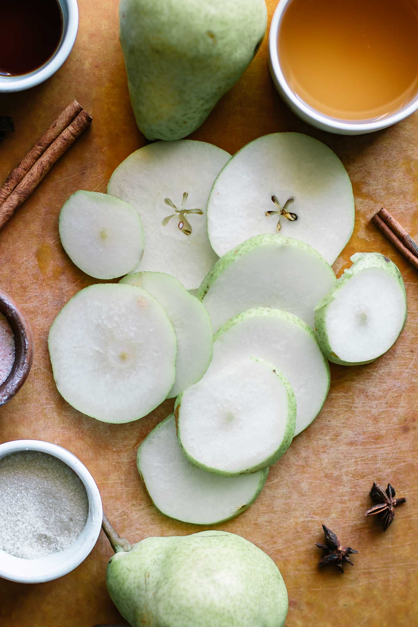 sliced pears on a cutting board with cinnamon and bowls of sugar and apple cider vinegar