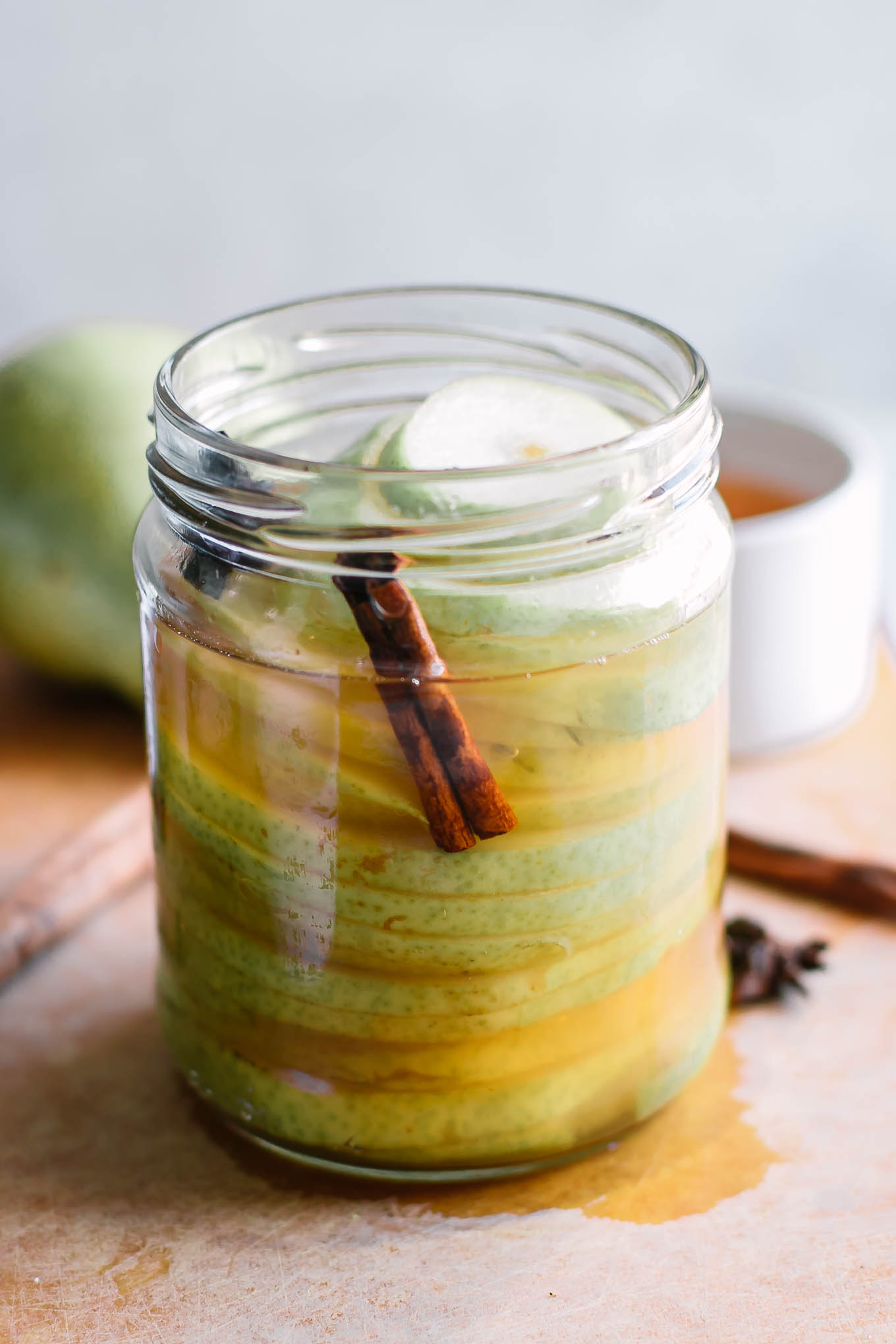 pickled pears in a jar with a cinnamon stick on a wood table