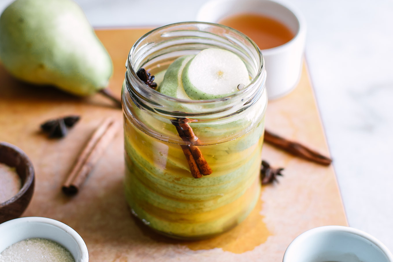 quick pickled pears in a jar on a wood table with pears in the background