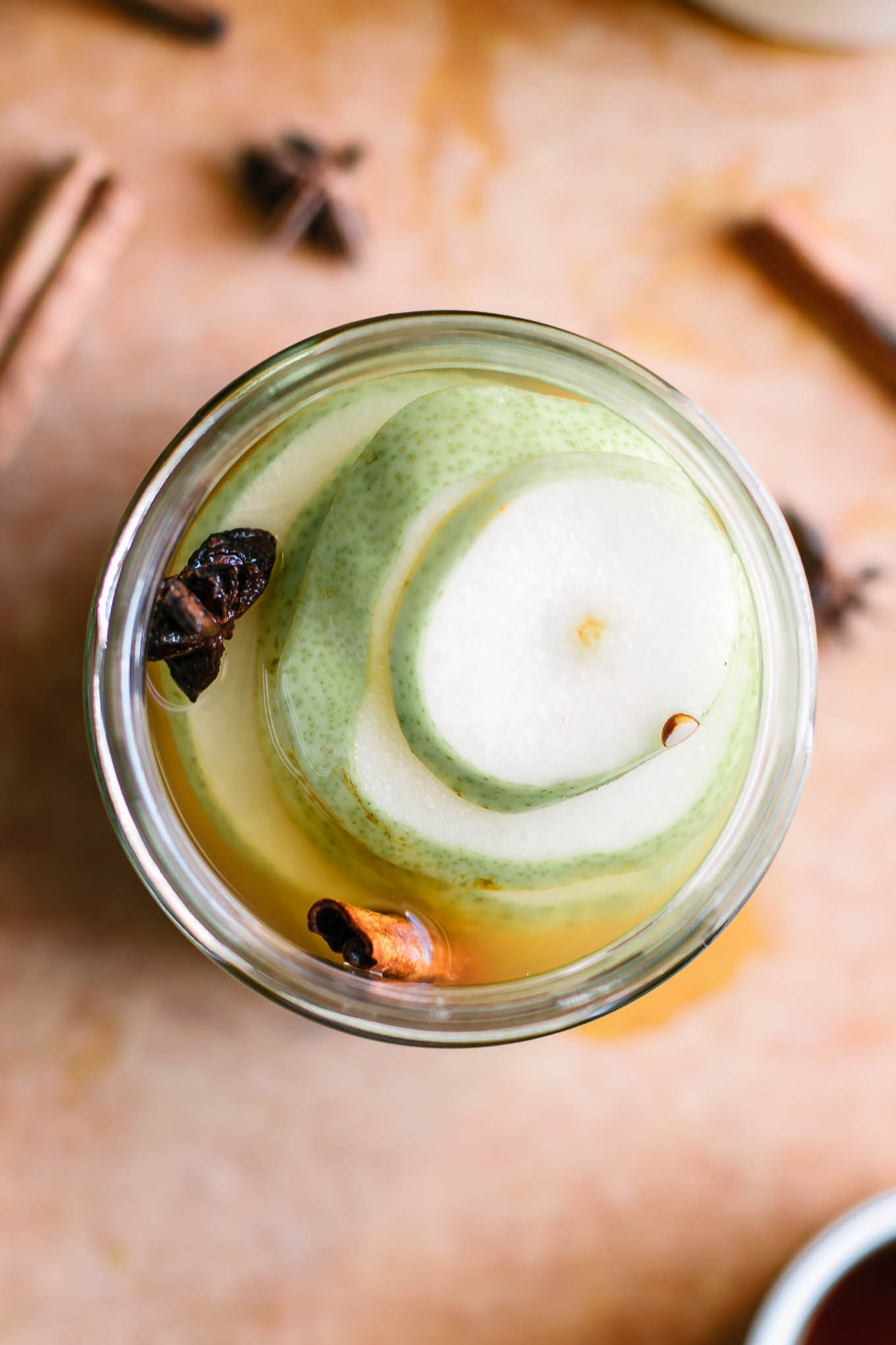 a close up shot of pickled pear slices in a glass jar on a wood table