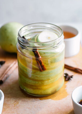 pickled pears in a jar with cinnamon sticks and star anise on a white table