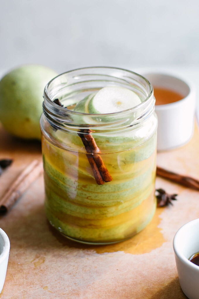 pickled pears in a jar with cinnamon sticks and star anise on a white table