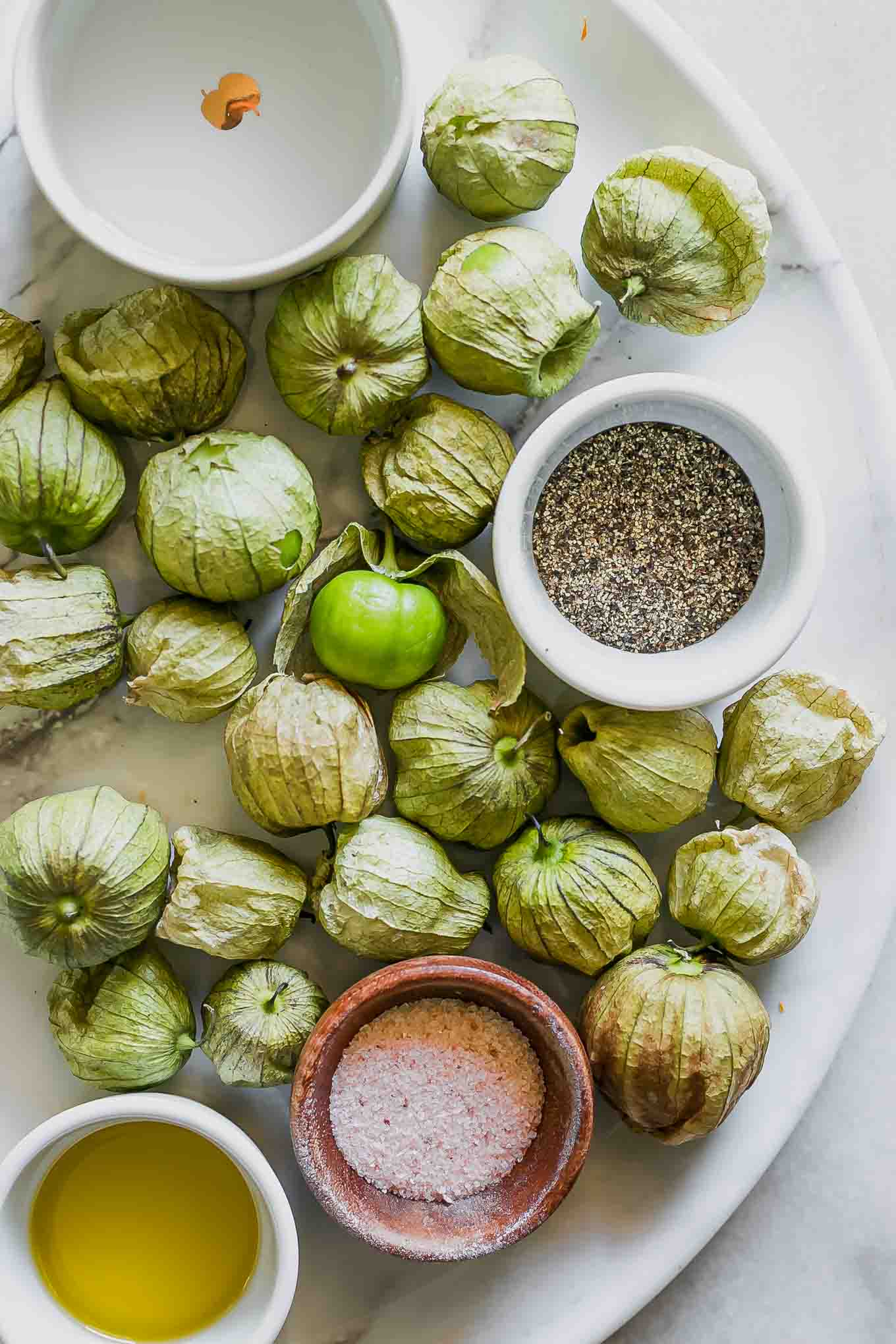 tomatillos on a white table with bowls of vinegar, salt, and sugar