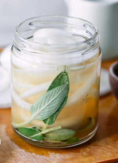 a jar of pickled onions with herbs on a wood table