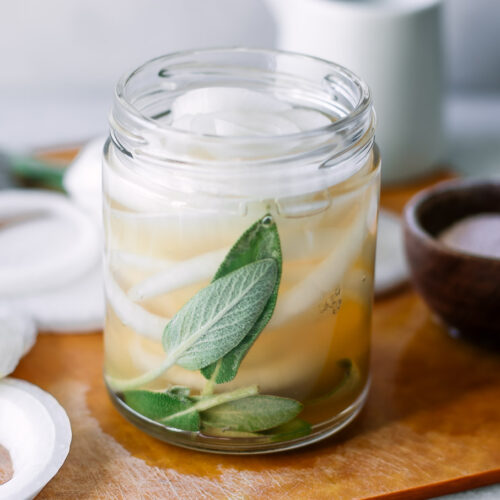 a jar of pickled onions with herbs on a wood table