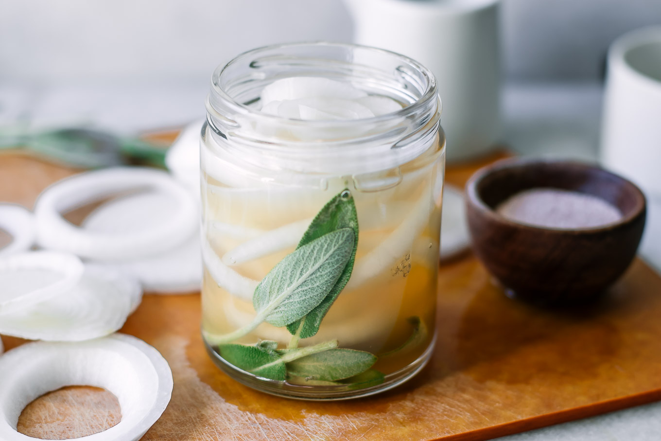 a jar of pickled onions with herbs on a wood table