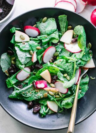 radish leaves salad in a black bowl with a gold fork