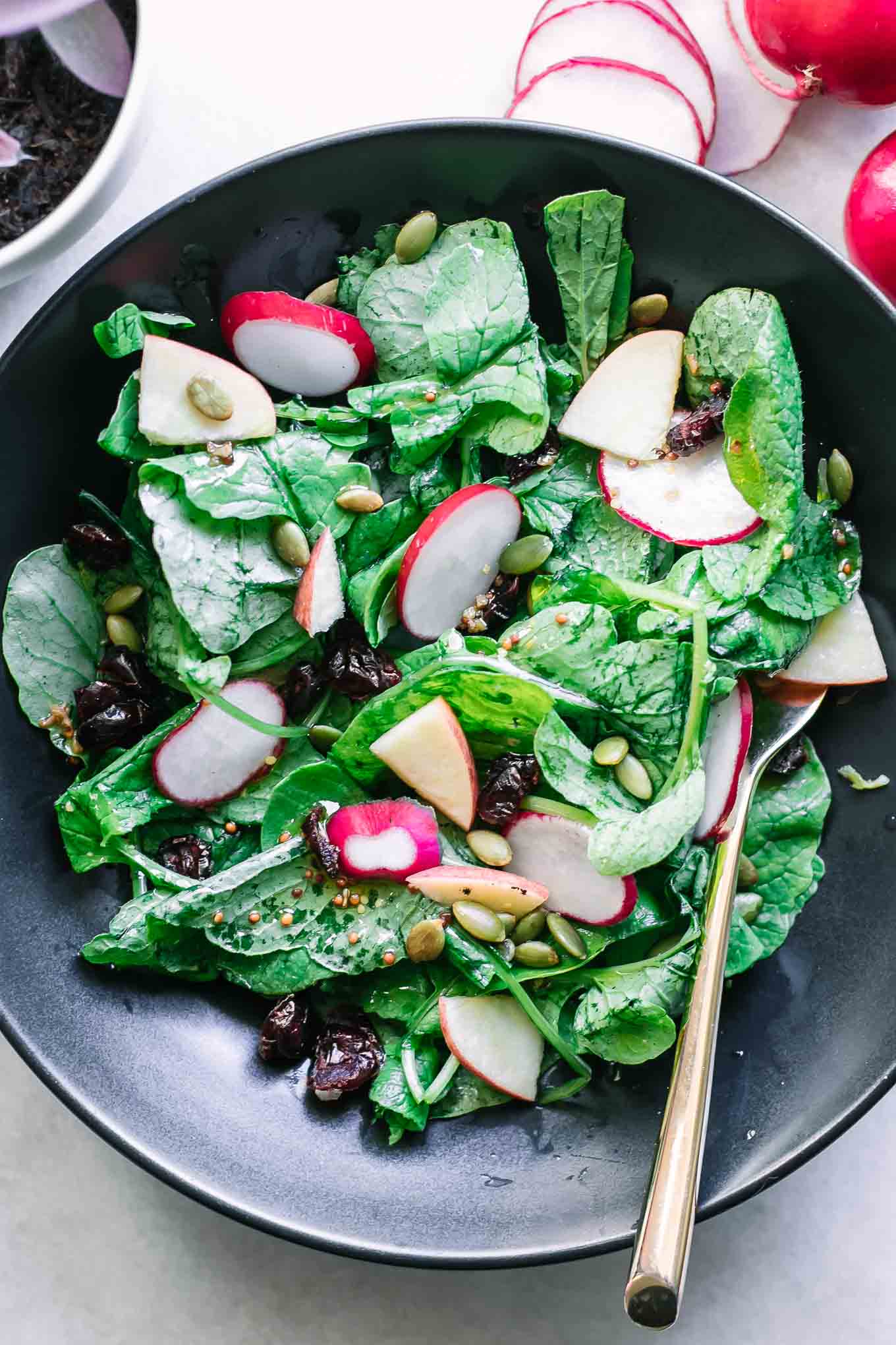 radish leaves salad in a black bowl with a gold fork