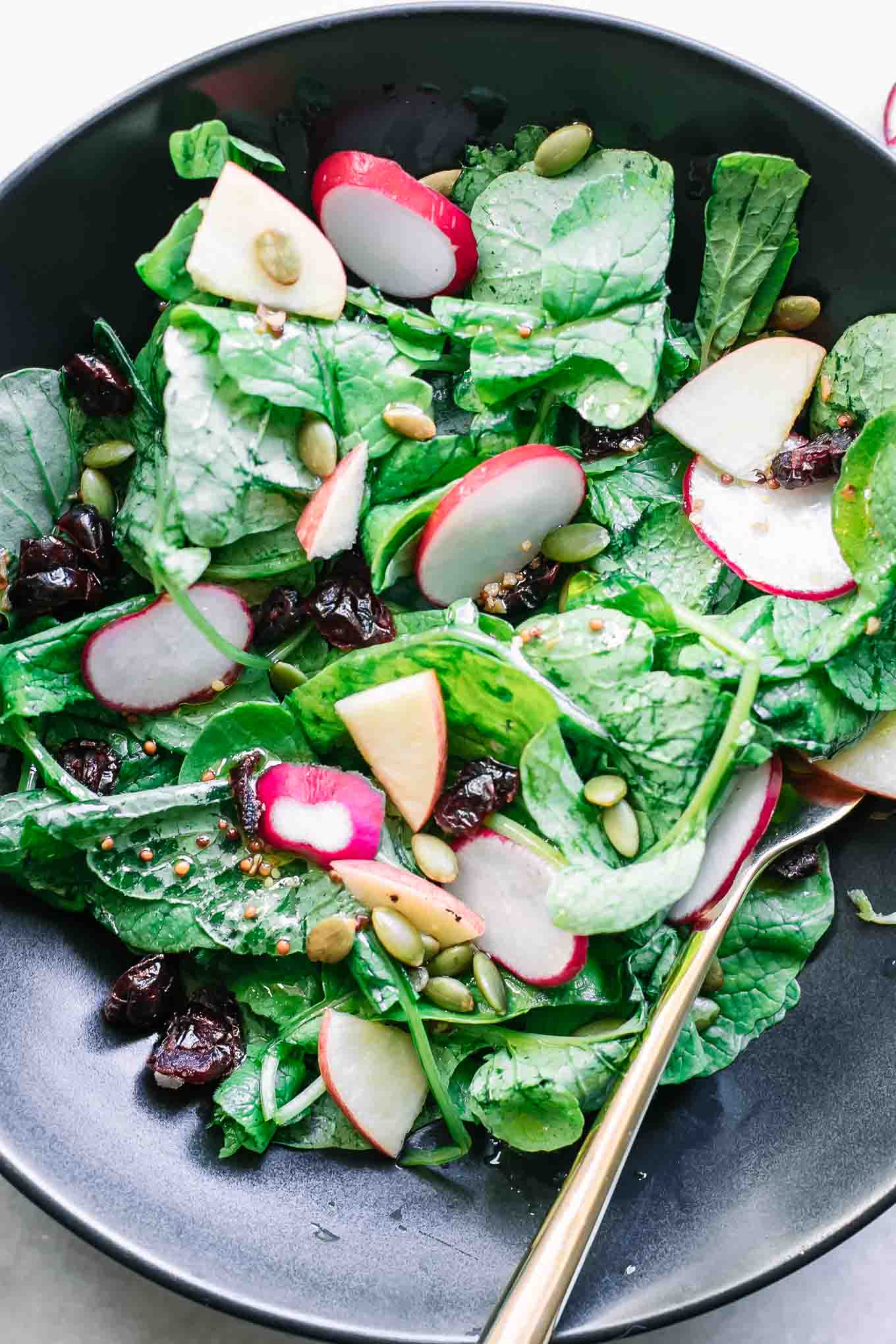 a black bowl with a salad made with radish leaves, sliced radishes, and sliced apples