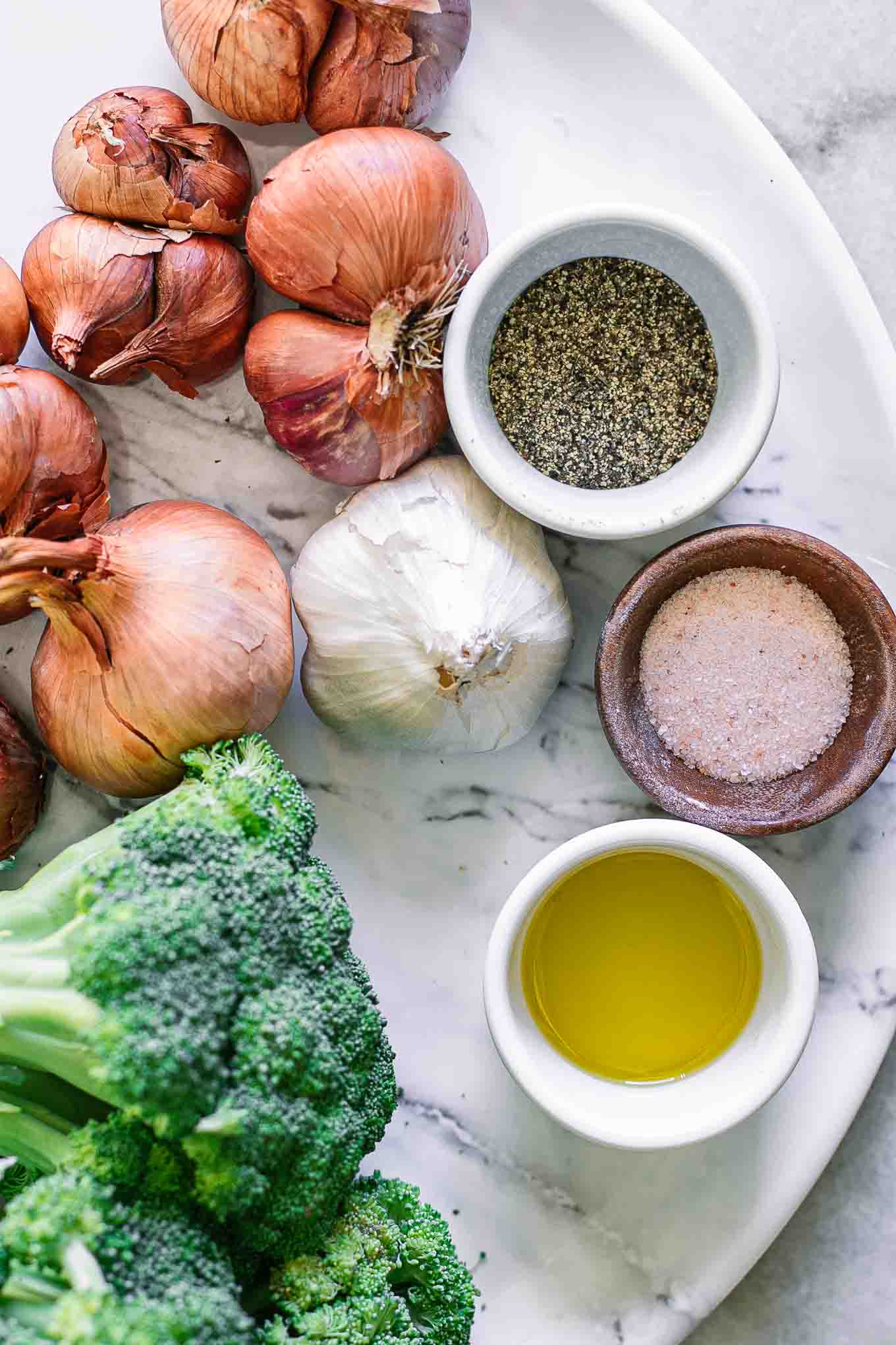 broccoli, shallots, garlic, oil, salt, and pepper on a white table