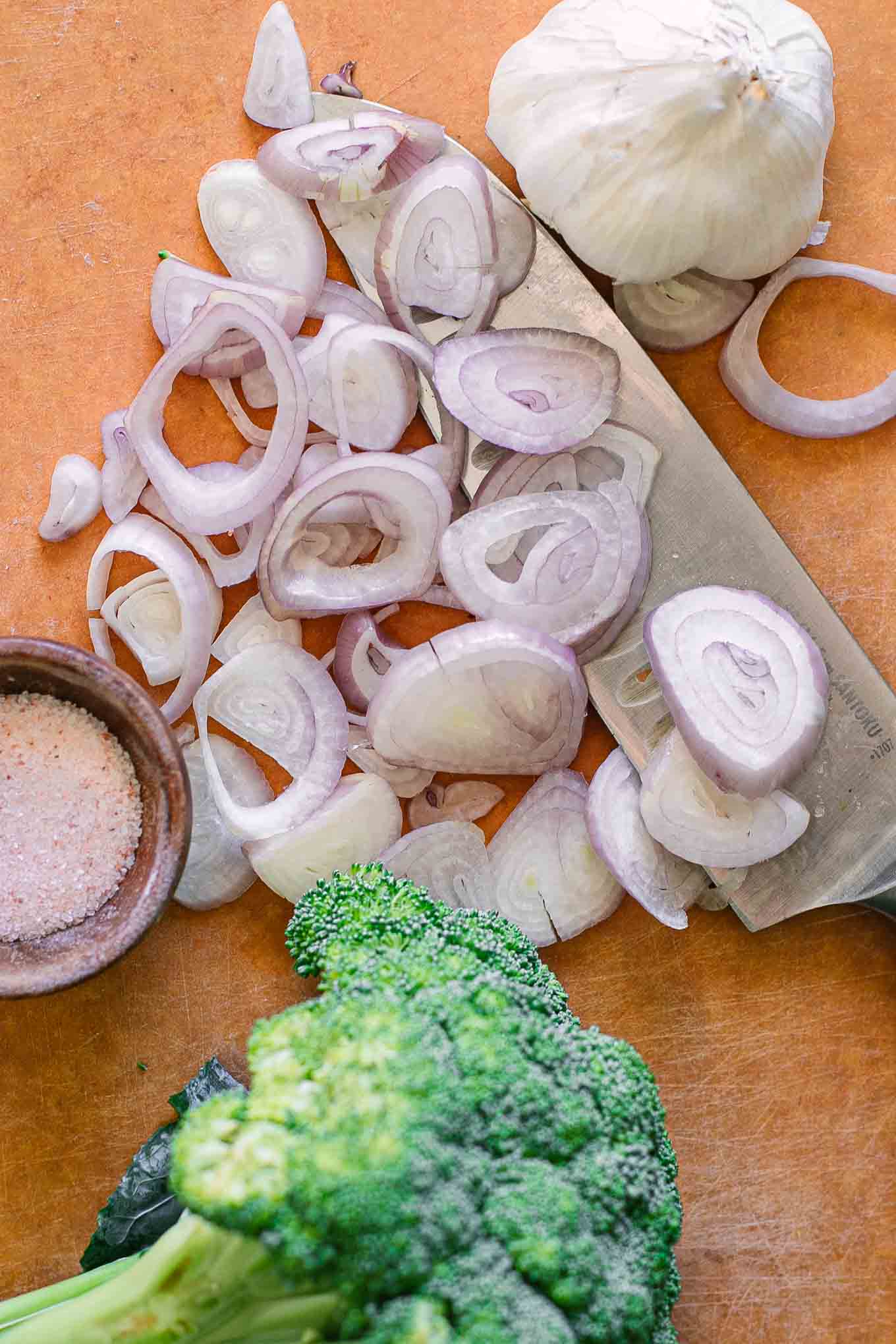 sliced shallots and broccoli on a wood cutting board