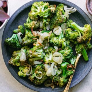 baked broccoli and shallots on a blue plate with a gold fork