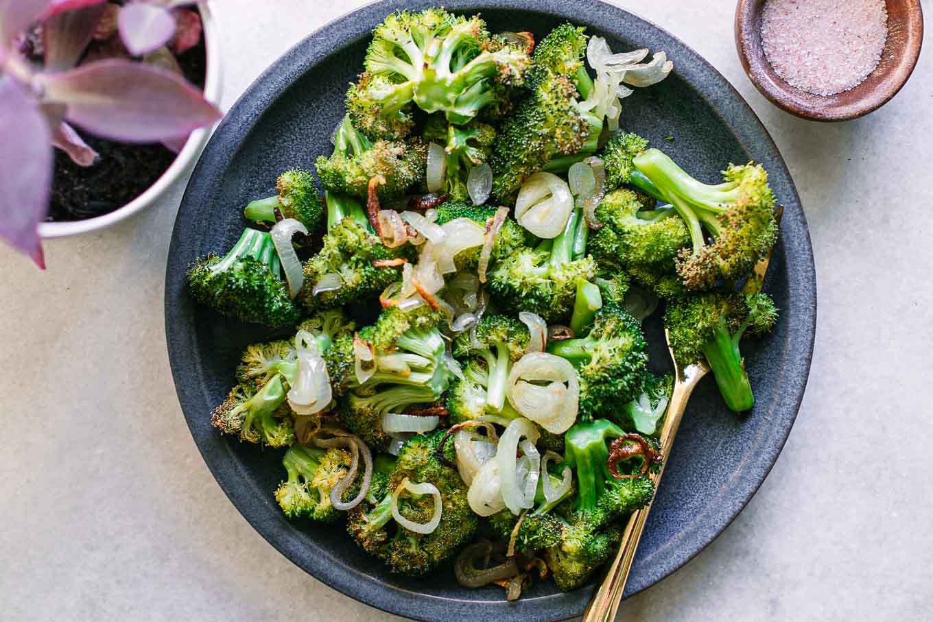 baked broccoli and shallots on a blue plate with a gold fork