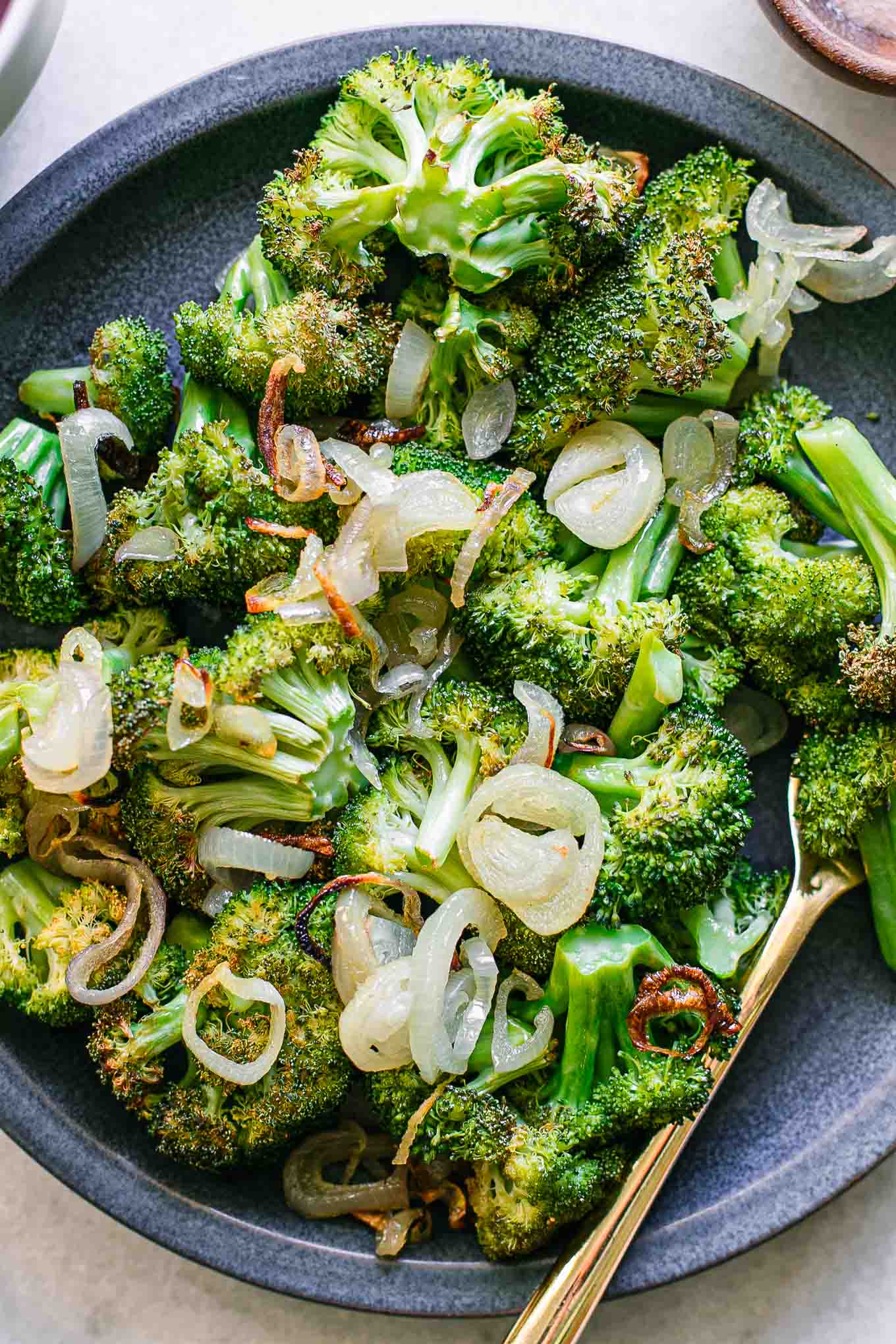 a close up photo of roasted broccoli and shallots on a blue serving dish