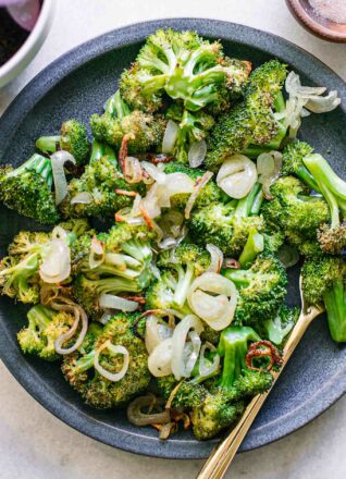 roasted broccoli and shallots on a blue side dish with a gold fork