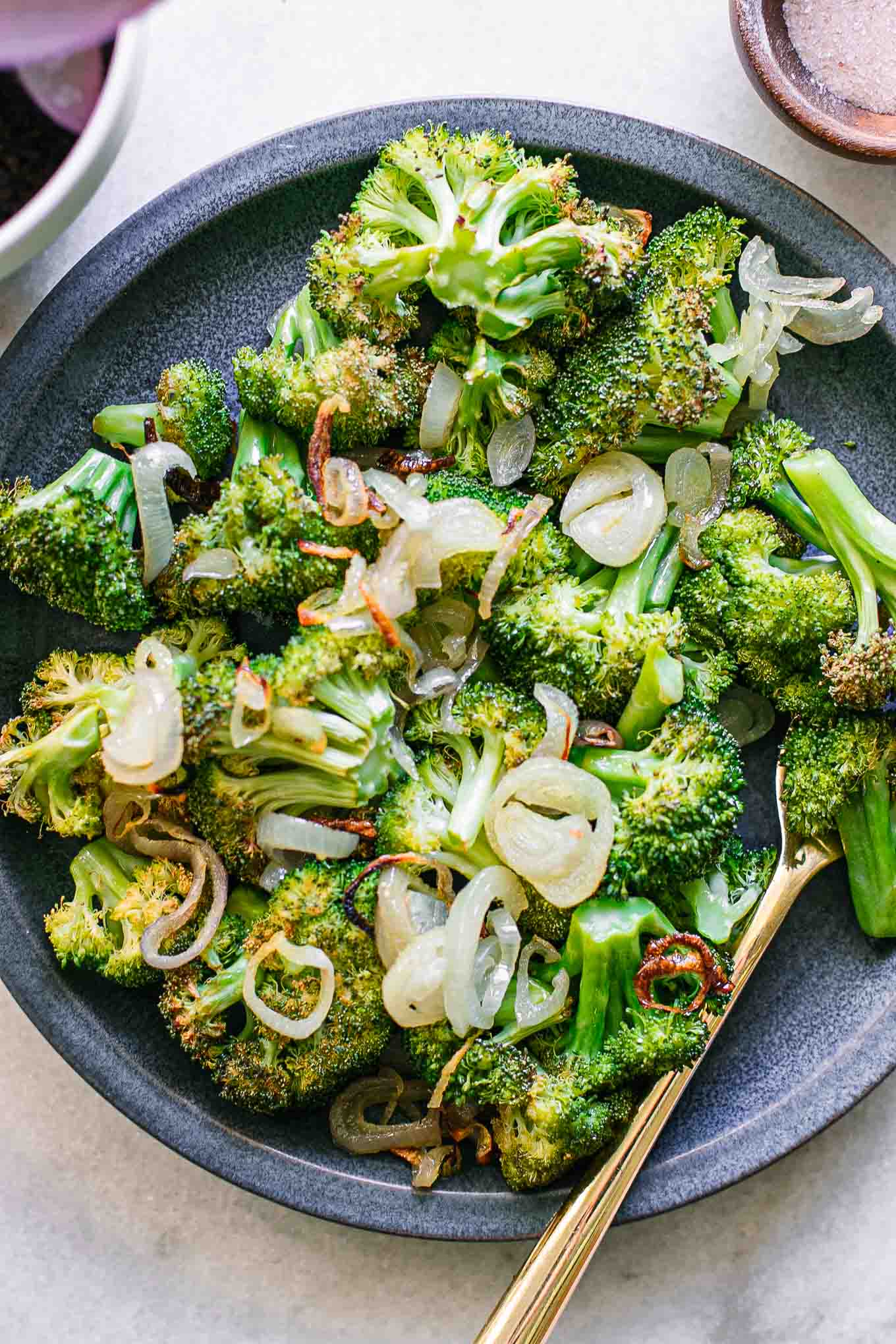 roasted broccoli and shallots on a blue side dish with a gold fork